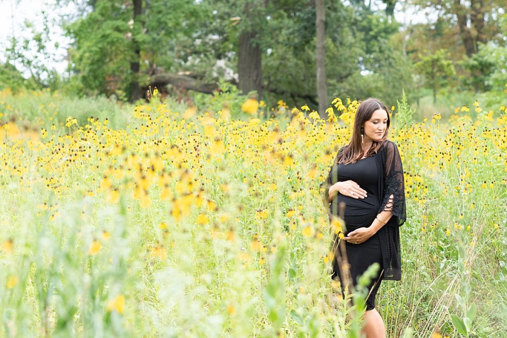 Mother to be poses in a blooming field of flowers