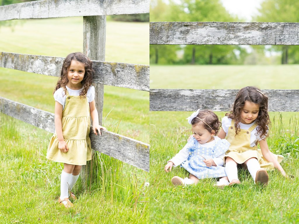 Two little girls one in a blue daisy dress and other in a yellow dress poses for photos in front of wooden fence in lexington tn
