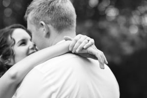 Woman and man embracing for a photo in black and white during their anniversary session. The woman's arms are wrapped around the man's neck and they are smiling at each other.