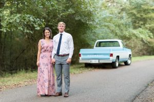Man and woman posing while holding hands in front of the back of a vintage blue Chevy truck