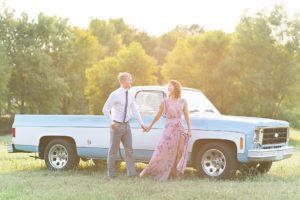 Couple holding hands in front of vintage Chevy truck in a green field