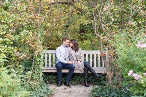 man and woman sitting on a bench for engagement photos. They are both looking at each other happily