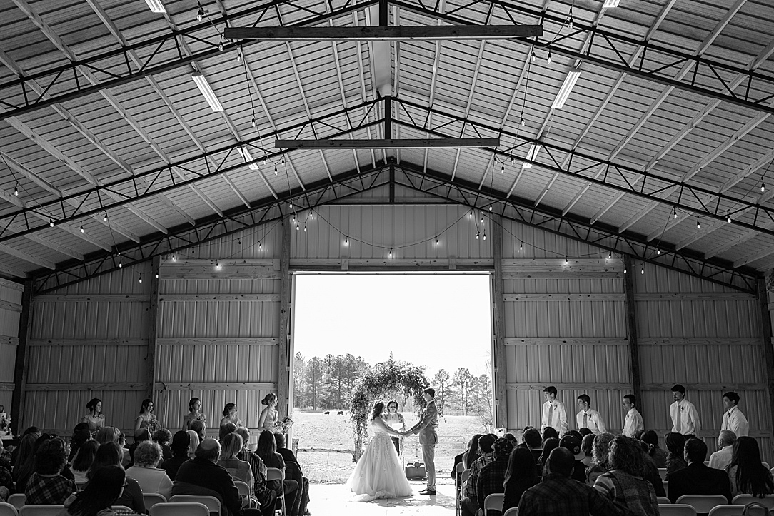 Photo of couple holding hands under floral arch at barn wedding