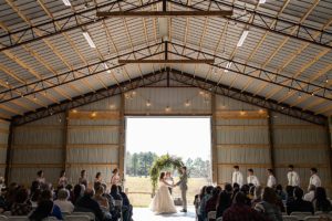Spring outdoor barn wedding with couple holding hands facing each other with bridal party surrounding them
