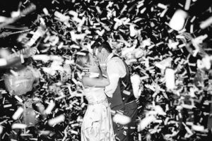 bride and groom kissing under confetti at wedding