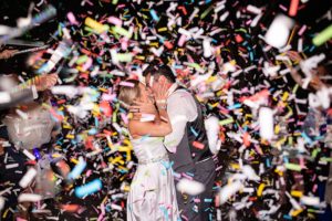 bride and groom kissing under confetti when leaving their wedding