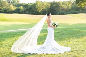 a bride posing with her bouquet and long veil flowing in the wind