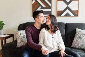 man and woman posing on a couch in their apartment for at-home engagement photos