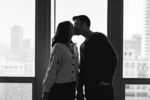 a man and woman kiss in their apartment during their at-home engagement photo session