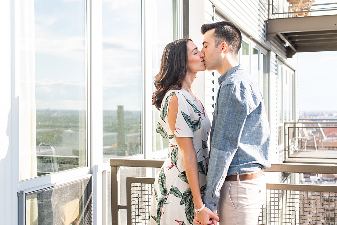 a man and woman kiss on their apartment balcony during their at-home engagement photos