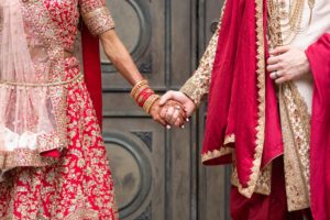man and woman hold hands while wearing traditional Indian wedding outfits