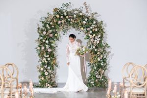bride poses in front of floral arch