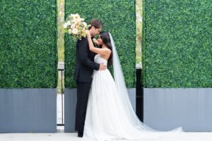 bride and groom pose in front of faux greenery wall